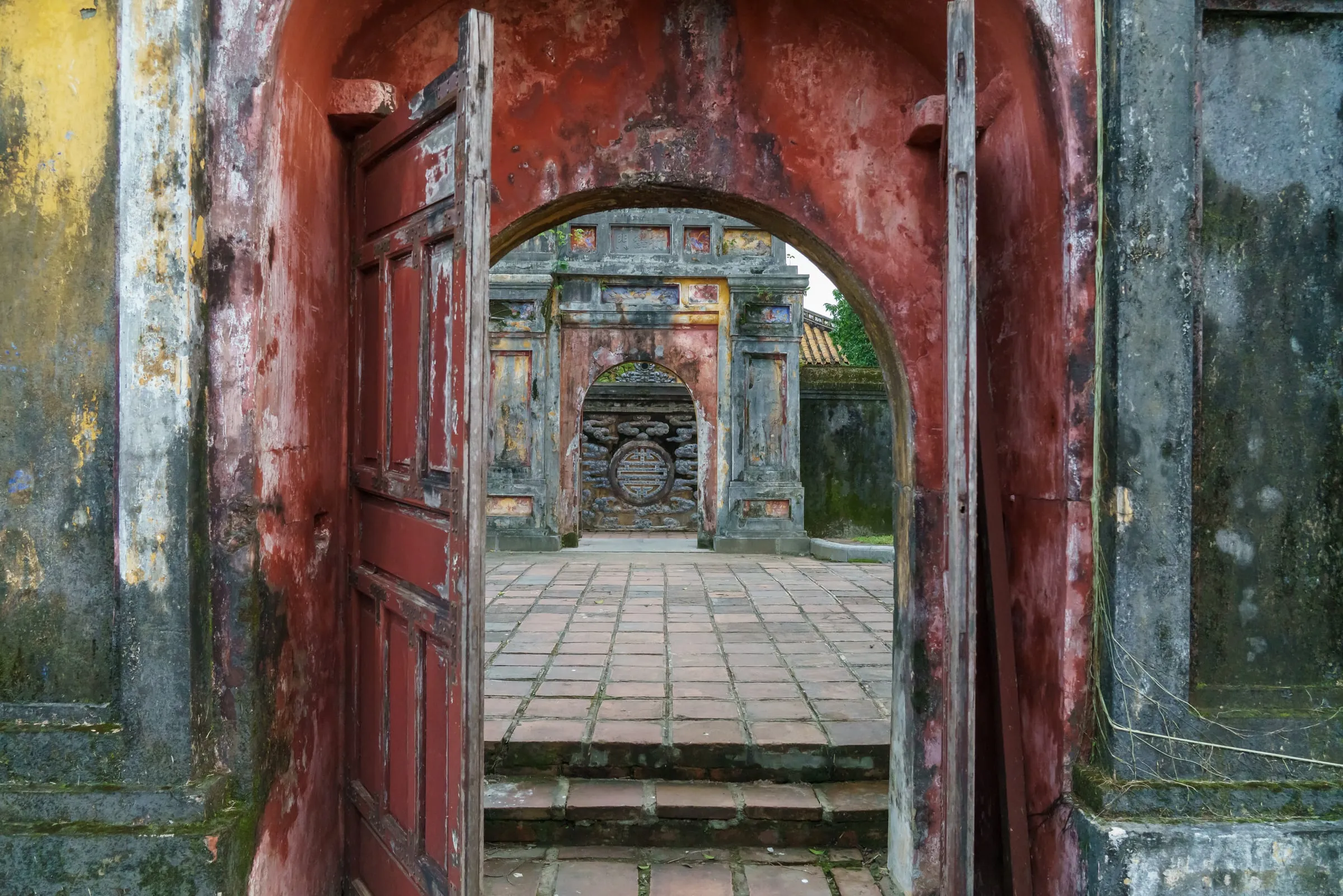 Gateway to a citadel courtyard in Huế — wooden doors set in a red-walled arch, with a stone courtyard and a second gate visible beyond.